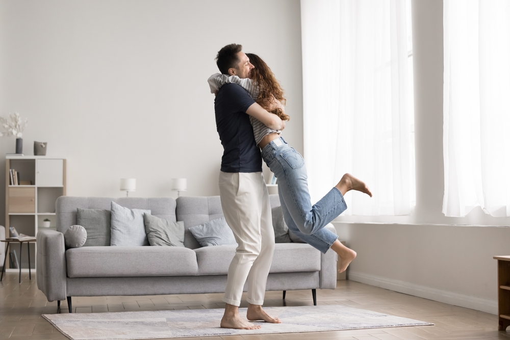 Couple celebrate relocation to new modern apartment, loving husband lifts his overjoyed wife, hugging, feel happy, start living together, enjoy move-in day to newly bought flat. Cohabitation, marriage