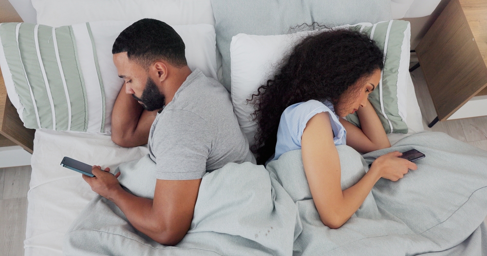 Couple, phone and conflict in bed, ignore and annoyed with reading, chat or social media addiction in home. Man, woman and doom scrolling with anger, fight or frustrated with mobile app on smartphone