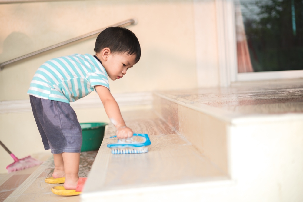 Asian boy about 2 years old doing chore by cleaning the house floor with hand brush