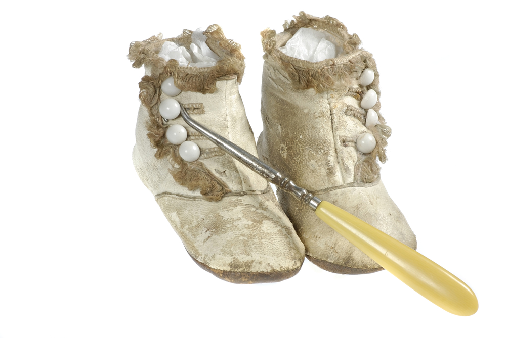Closeup of a pair of antique high-top, button top baby shoes and a button hook, isolated on white background