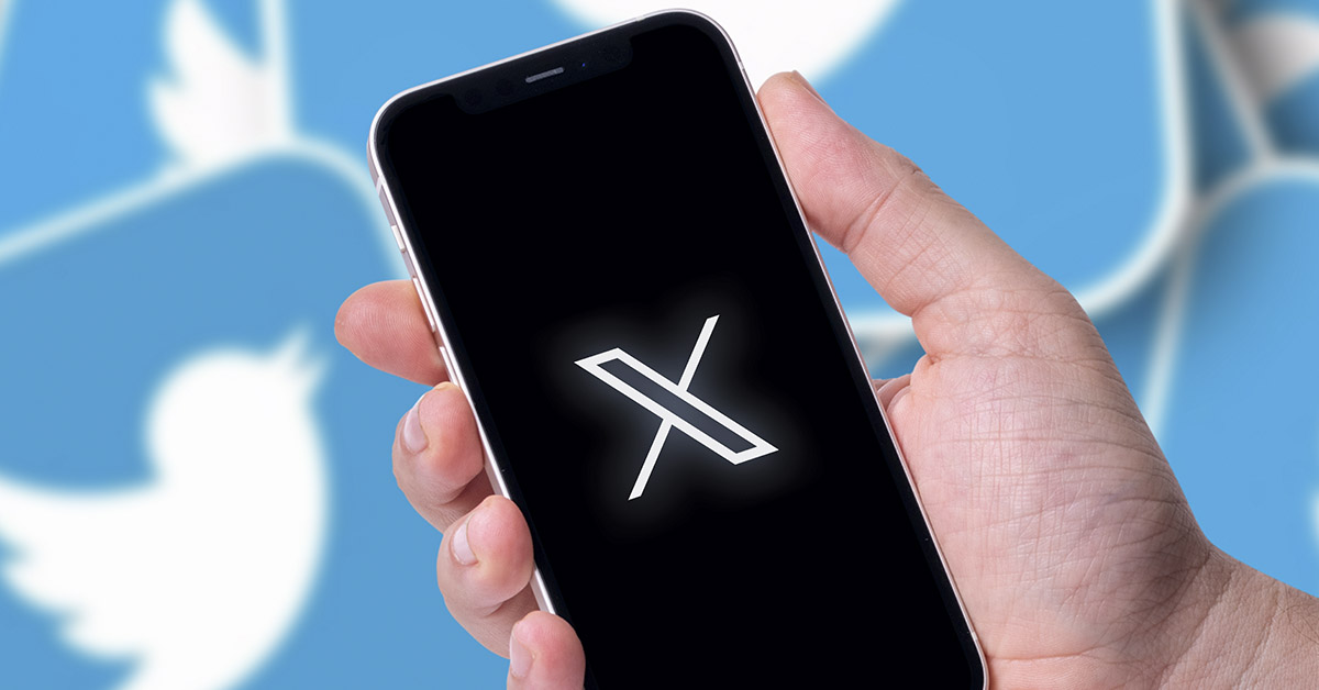 Person holding a phone with X social media logo on it. Twitter bird in background