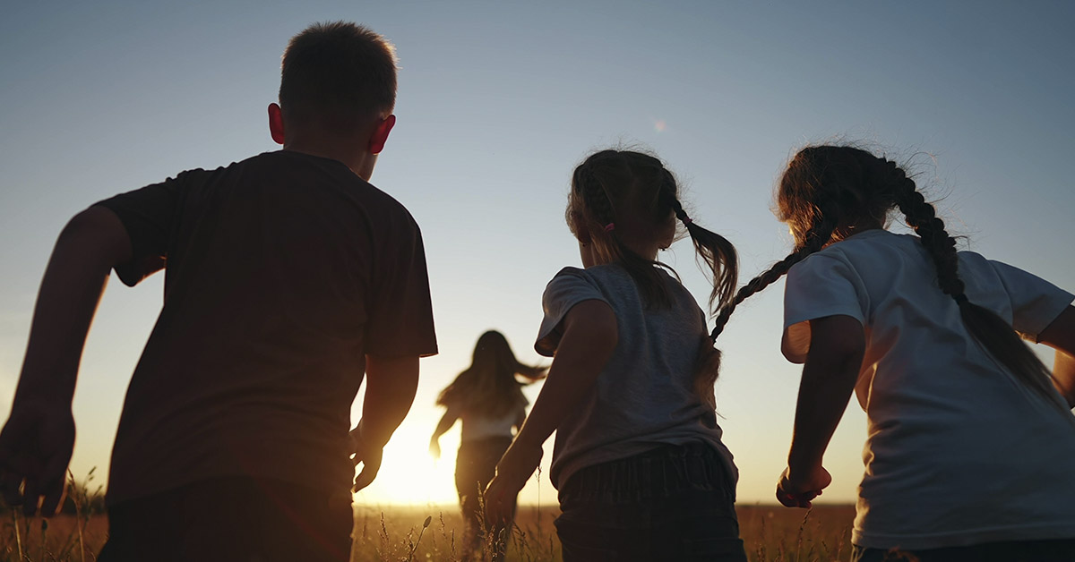silhouette of children running in field while sun is setting