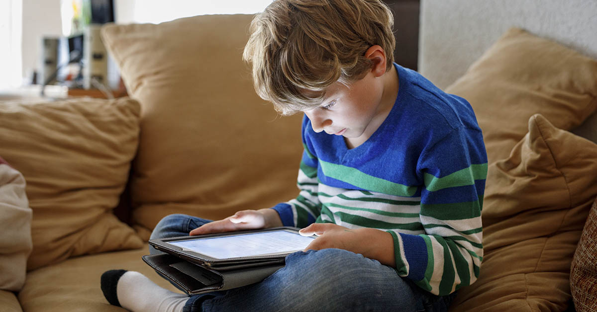Child sitting on couch using a tablet. Screen time concept