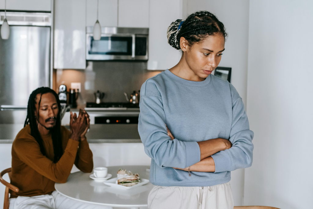 Upset woman with crossed arms while a man sits nearby, demonstrating withdrawal patterns that develop when past trauma makes communication feel unsafe.