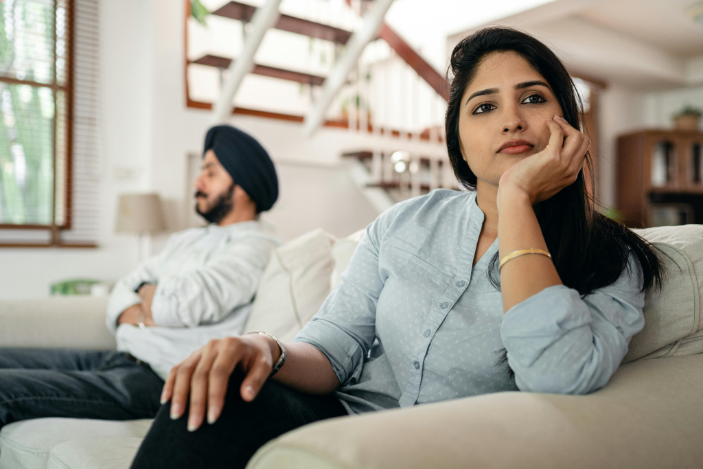Woman looking pensively away from distant male partner, showing emotional disconnect when couples who don't openly talk about their needs expect mind-reading instead of clear communication.
