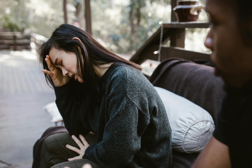 Woman sitting with head in hand while man sits close by, depicting the emotional isolation that builds between both partners from accumulated relationship resentment.
