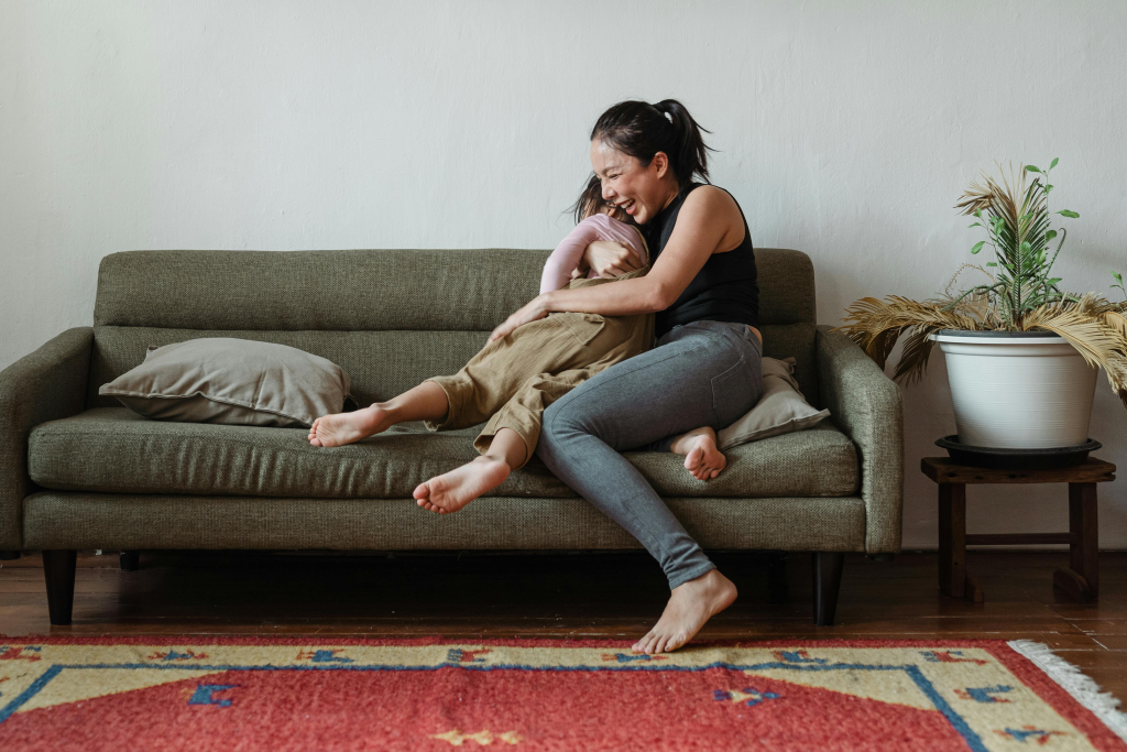 Mother holding and smiling with her child on a couch, demonstrating the warm, nurturing parenting style that research shows helps prevent narcissistic behaviors in children, contrasting with abusive or overly permissive approaches that can contribute to problematic development.