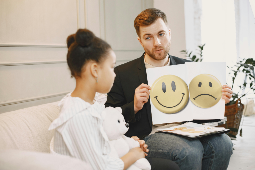 Therapist holding cards with happy and sad face emoticons during a session with a child.