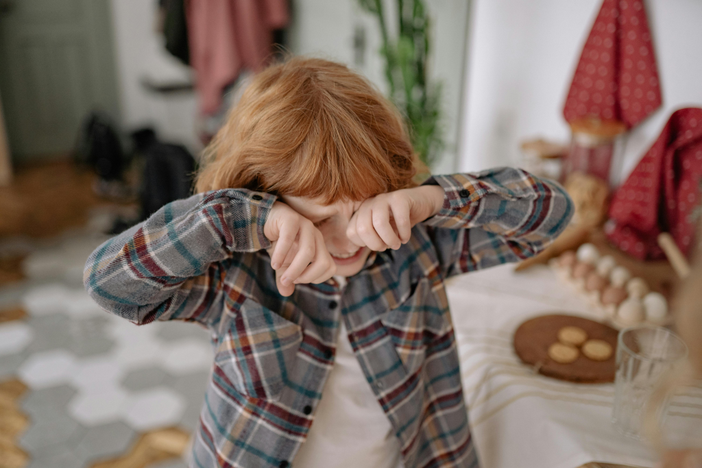 Young child with hands covering face, appearing distressed.