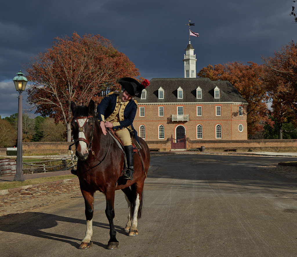 Colonial interpreter on horseback in front of historic brick Capitol building where America's founders once governed.
