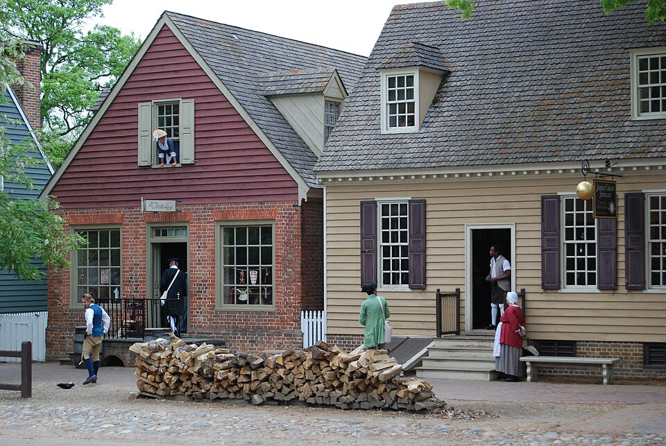 Costumed interpreters in period dress demonstrating daily life outside authentic colonial buildings where history comes alive.
