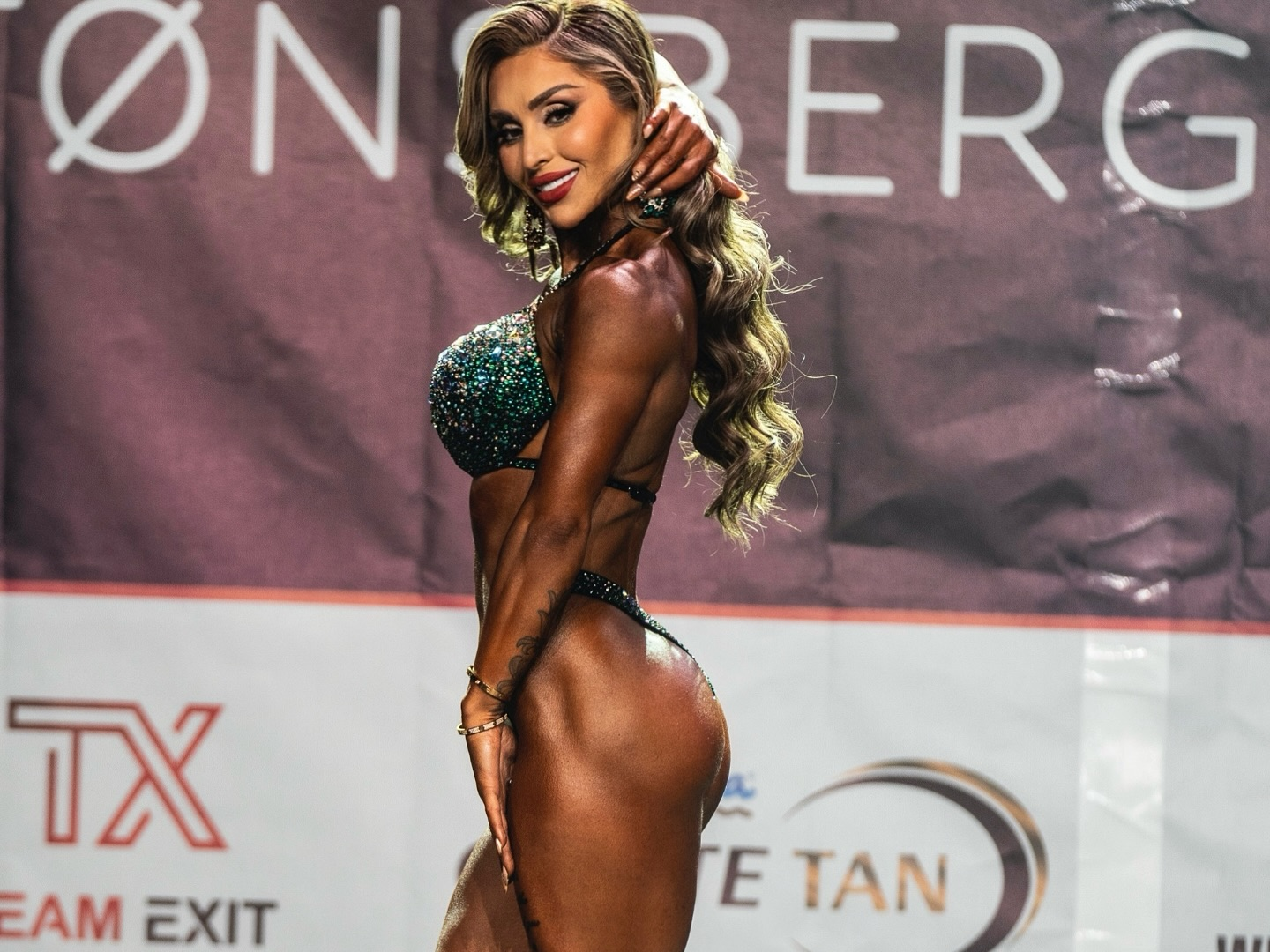 Roya Karimi posing side profile at a bodybuilding competition.