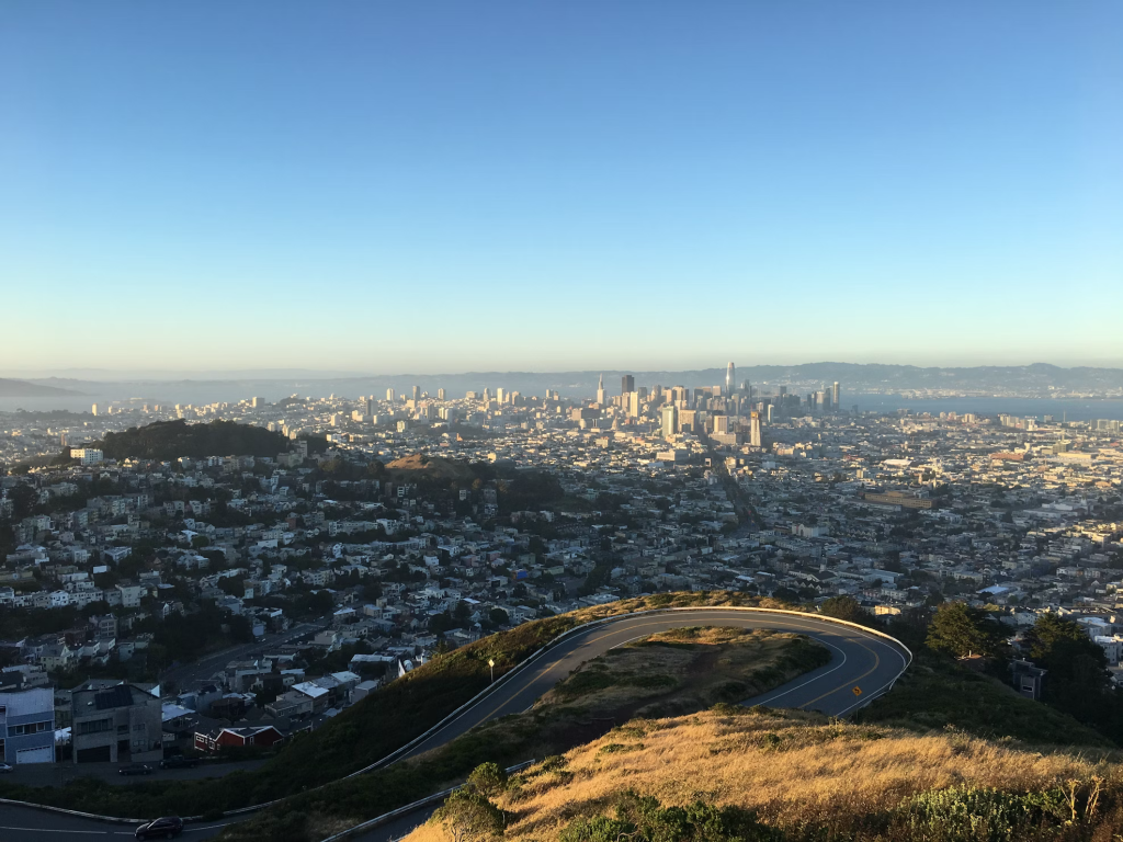 Aerial view of San Francisco's downtown skyline and residential neighborhoods with the city's famous hills stretching toward distant mountains.