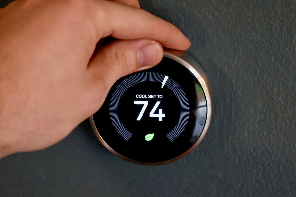 Hand adjusting temperature on smart thermostat to save energy and money. Green tech!