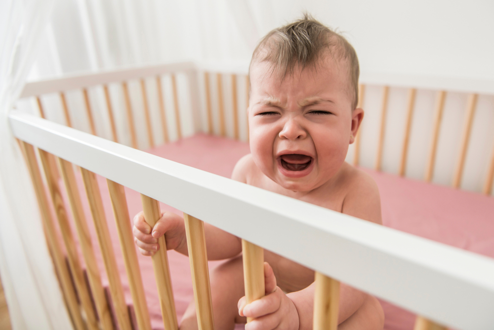 The cute baby cries and calls mum from a bed
