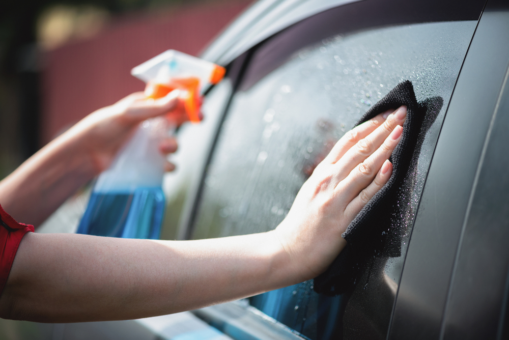 Cleaner is cleaning a car window glass with a rag and detergent close up.