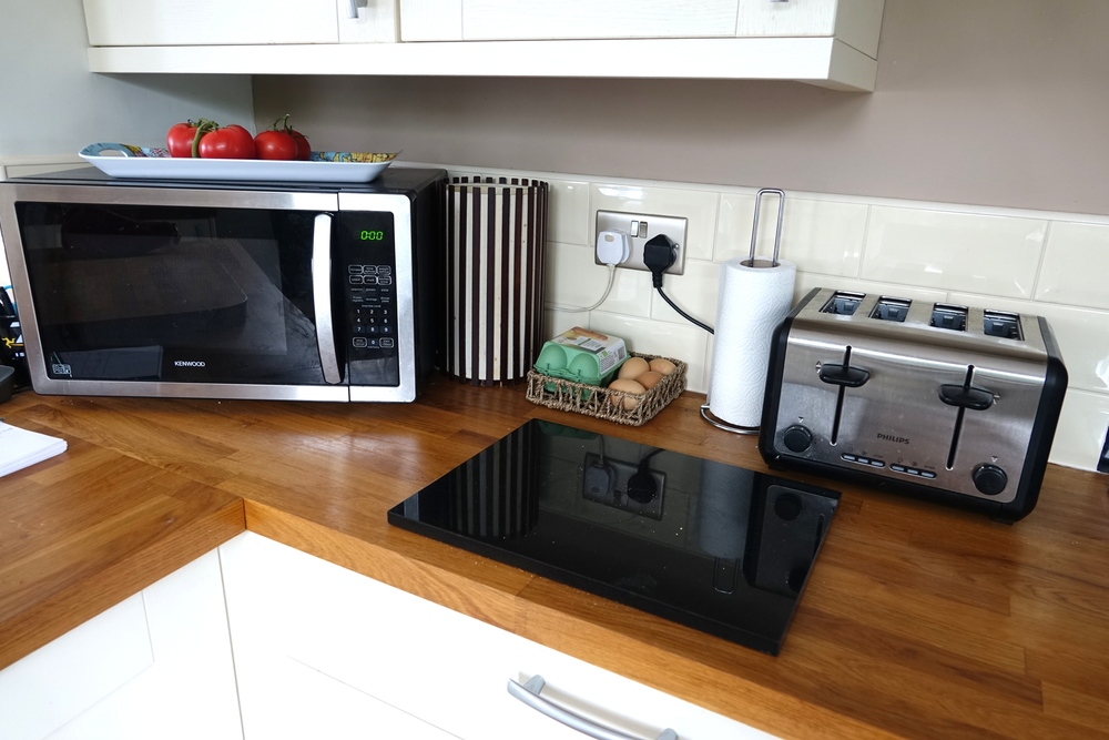 Dartmoor England. Domestic kitchen with micro-wave oven tomatoes on top. Toaster, kitchen towel role. Basket of eggs, Lamp. Black marble cutting board. Wall plugs.  Hardwood work surface 