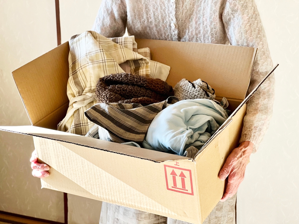 Hands of an elderly woman holding a cardboard box containing clothes