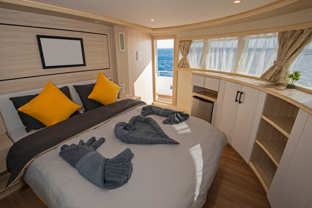 Interior of large suite cabin bedroom on luxury sailing yacht with double bed and panorama window