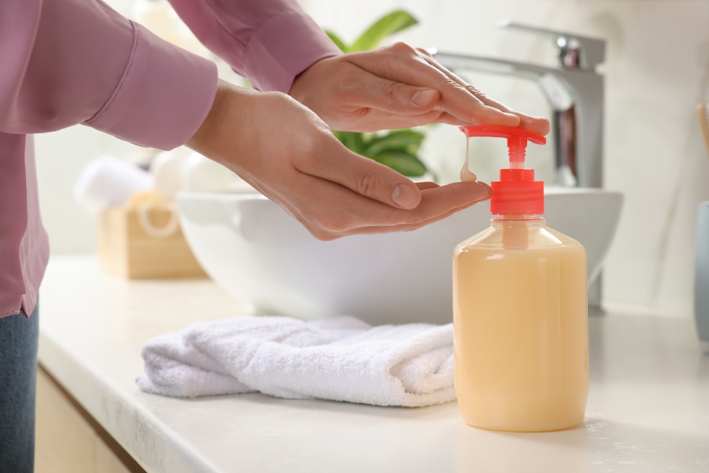 Woman using liquid soap dispenser in bathroom, closeup
