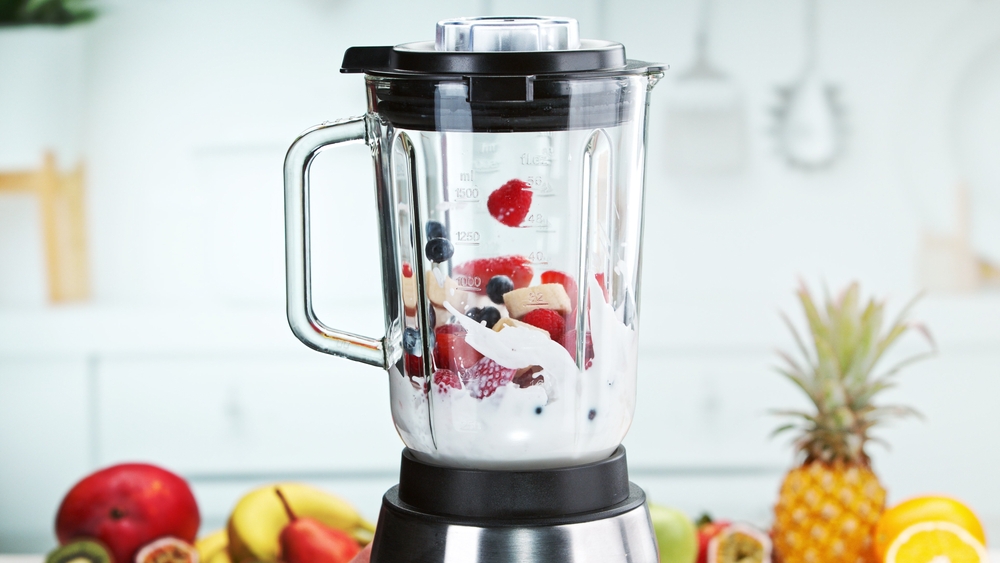 Mixing pieces of fruits with milk and in blender. Preparation of healthy drink.