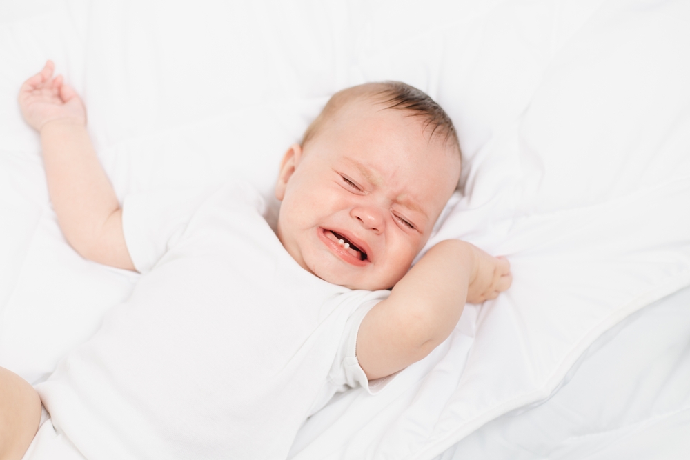 The baby is crying in his crib . The baby 's teeth are teething . Colic in babies . Hungry baby . Baby on a white background
