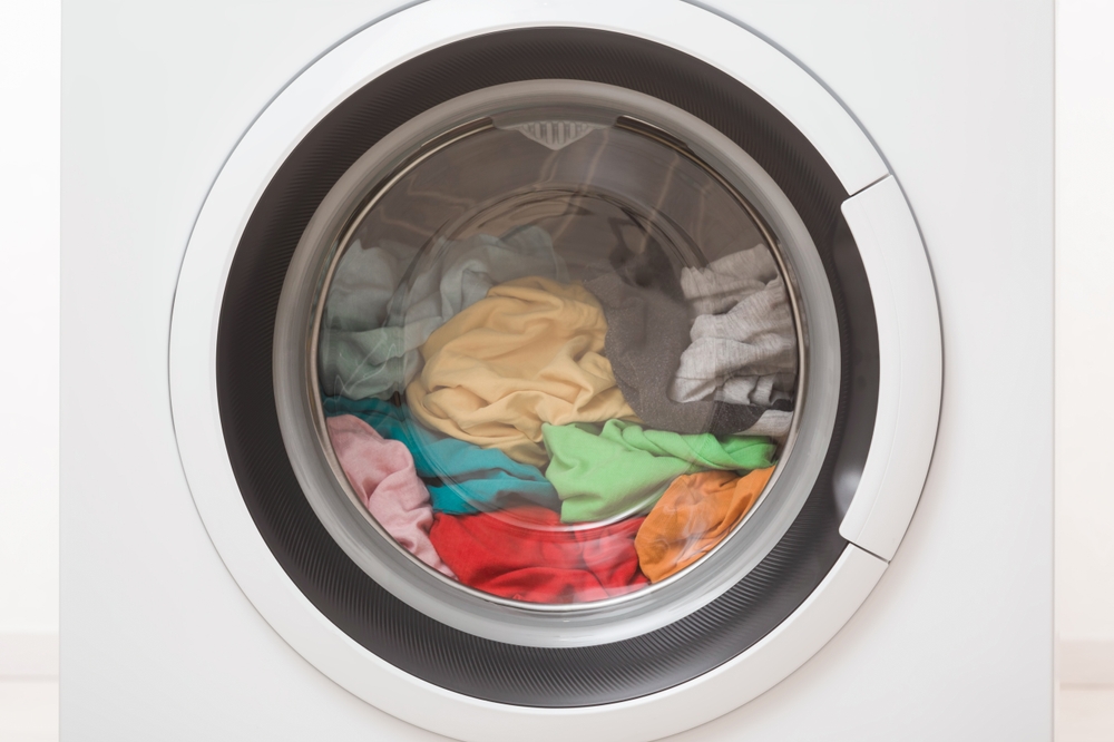 Closed washing machine full of colorful clothes. Closeup. Front view.
