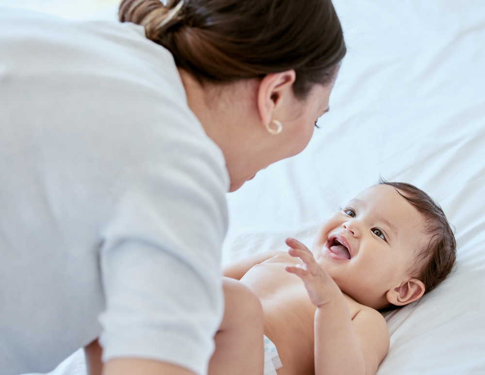Smile, mom and baby on bed with playing, bonding and laughing together with happy toddler. Home, mother and infant girl relax in bedroom with fun for growth, love and support in child development
