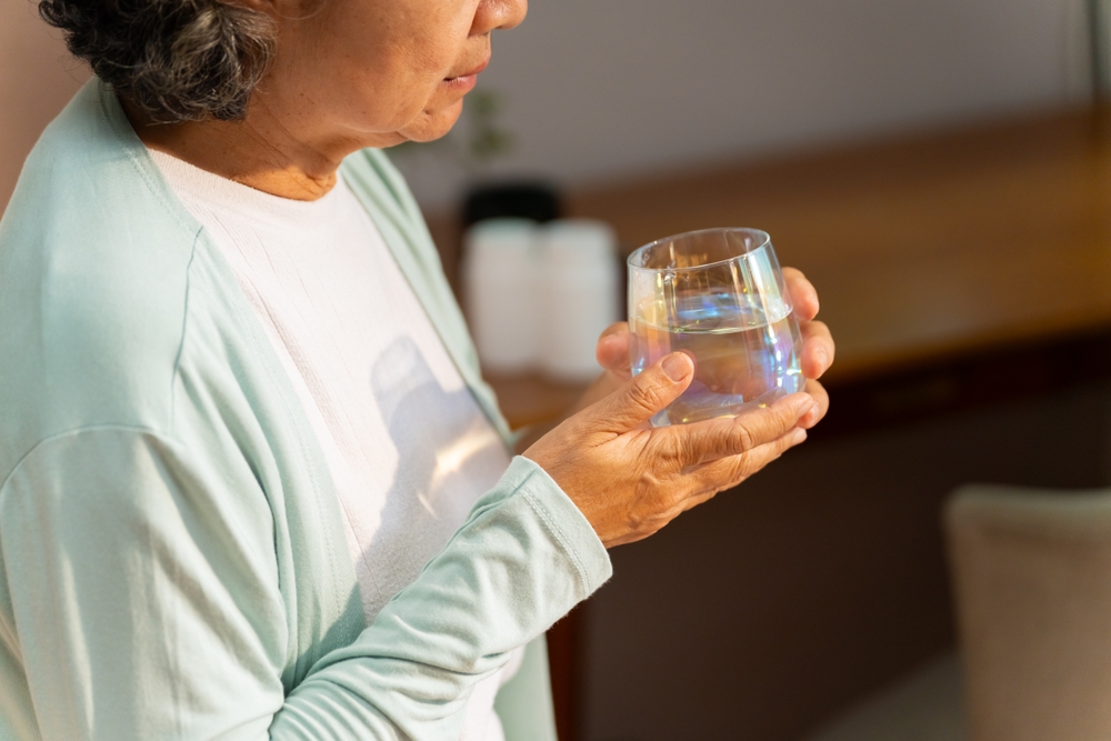 Asian senior mature woman drinking water from a glass after wake up on the bed in the morning. Elderly retired woman taking medicine or vitamins complex supplement at home. Healthcare concept.