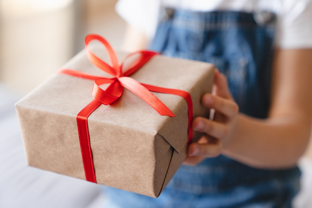 Giving receiving presents concept. Small kid child receiving giving gift box present with red ribbon on Christmas birthday holiday event celebration, closeup cropped shot