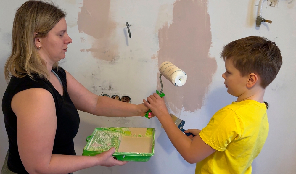 Mom and her little son are doing repairs in the room, they painted the wall with a brush and a roller. A friendly family, the new children's room in the house. Wall painting. Renovation concept