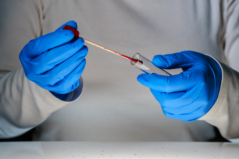 Forensic technician taking DNA sample from blood stain with cotton swab on murder crime scene.