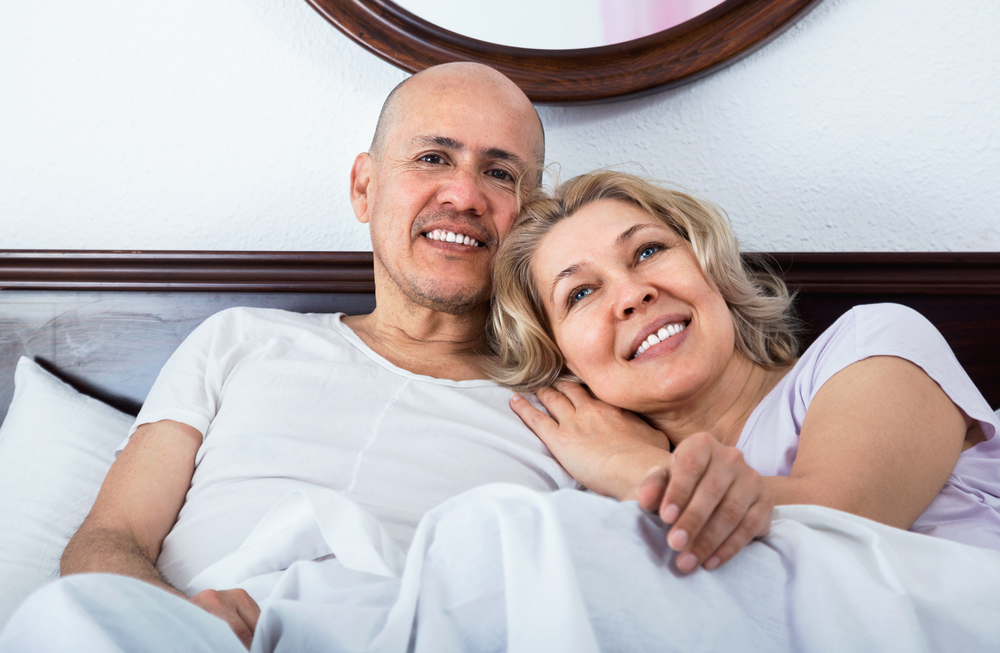 Positive happy smiling mature loving couple lounging in bed after awaking cuddling