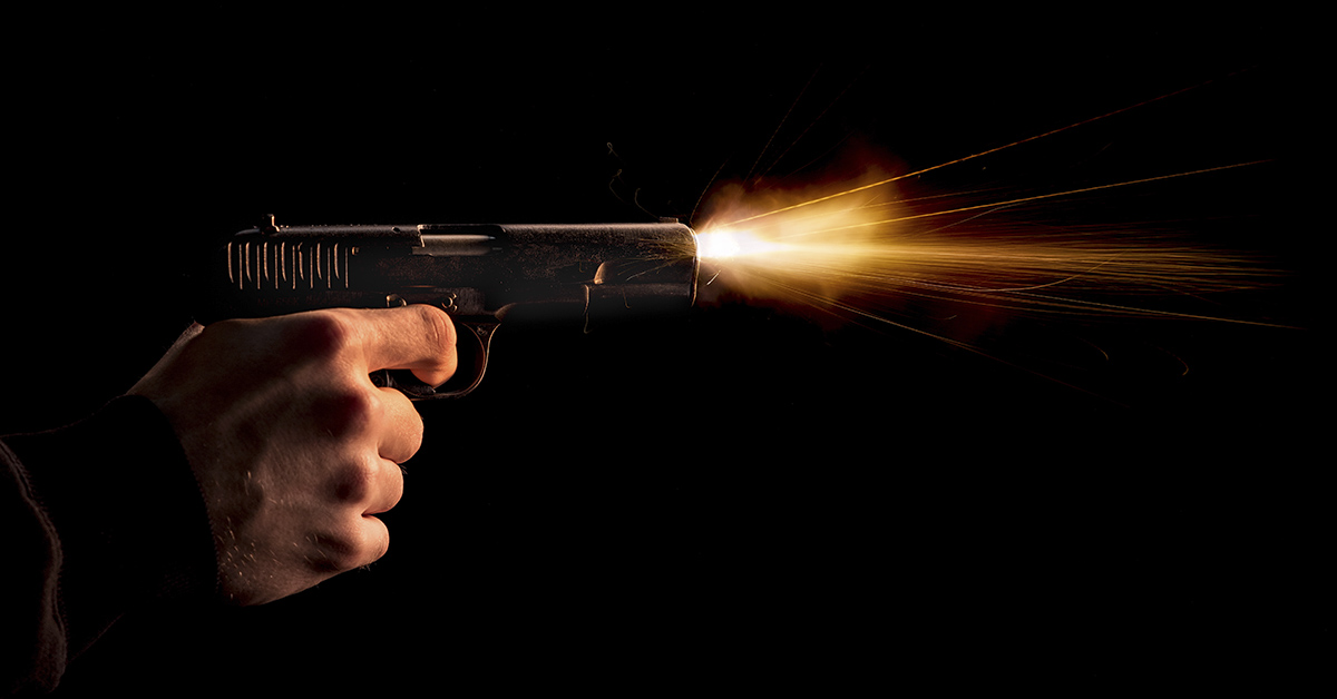 gunshot being fired from pistol. Dark background with prominent mussel flash