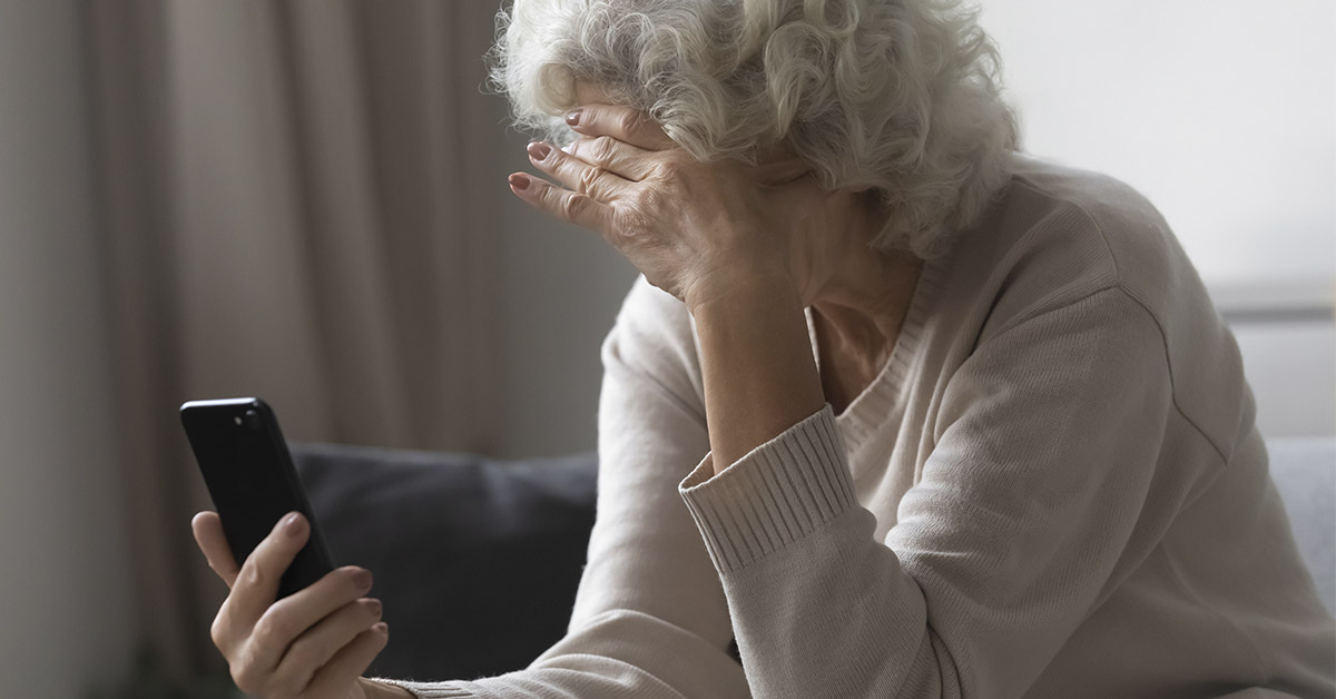 elderly woman looking at her smartphone in distress. Her hand is placed on forehead