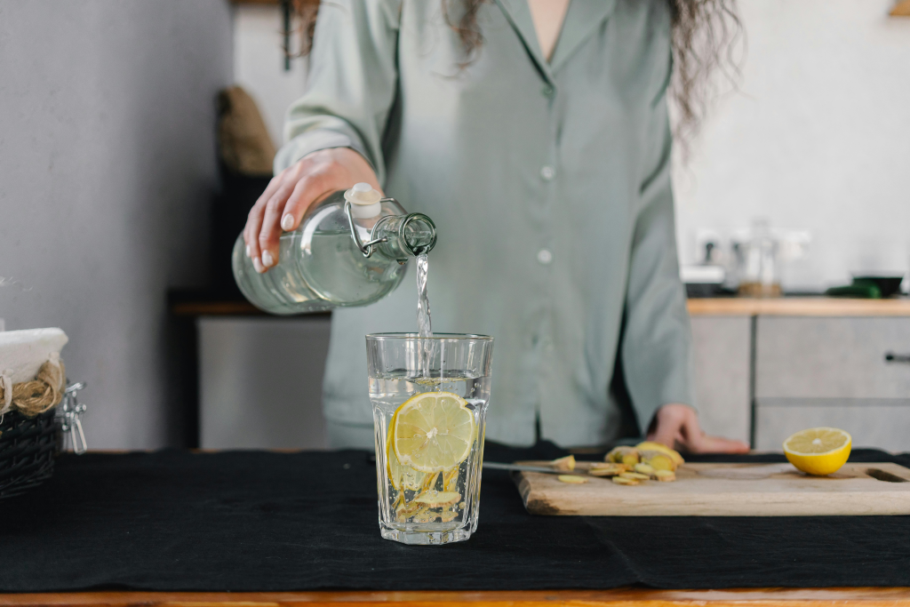 Someone pours water into a glass where fresh lemons wait, creating an everyday ritual that uses citrus for natural hydration.