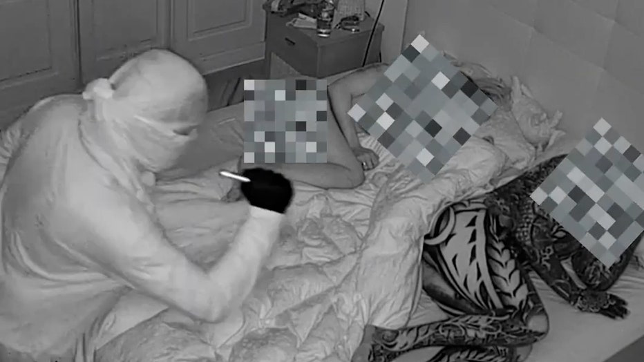 Black and white security footage showing masked intruder in bedroom with sleeping people, areas pixelated for privacy.