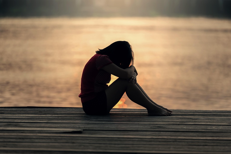  Solitary figure sitting on a dock at sunset, contemplating while facing the vast water alone.