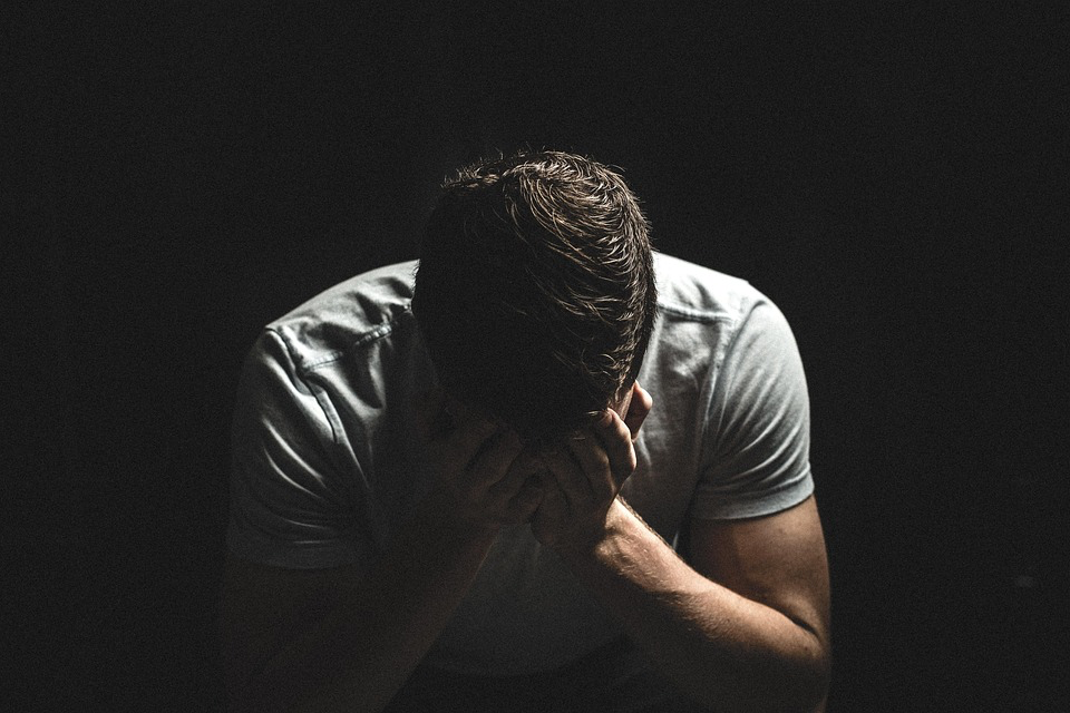 Person in the dark cradling their head, depicting the weight of emotional pain and isolation.