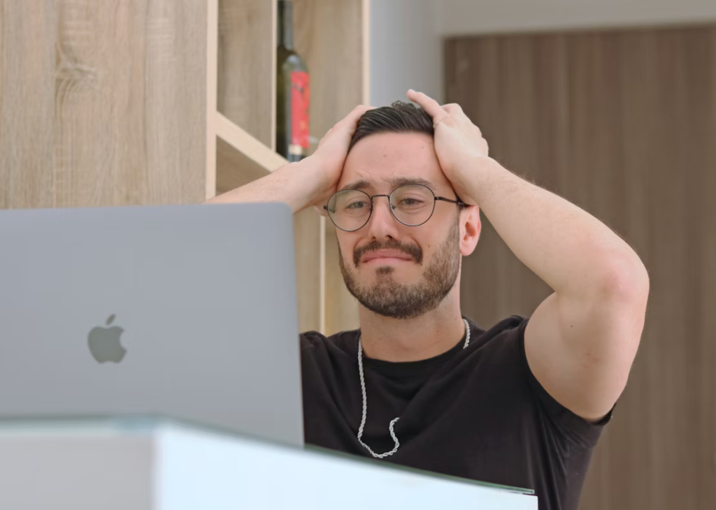 Frustrated person at a laptop holding their head, displaying signs of stress and mental exhaustion.