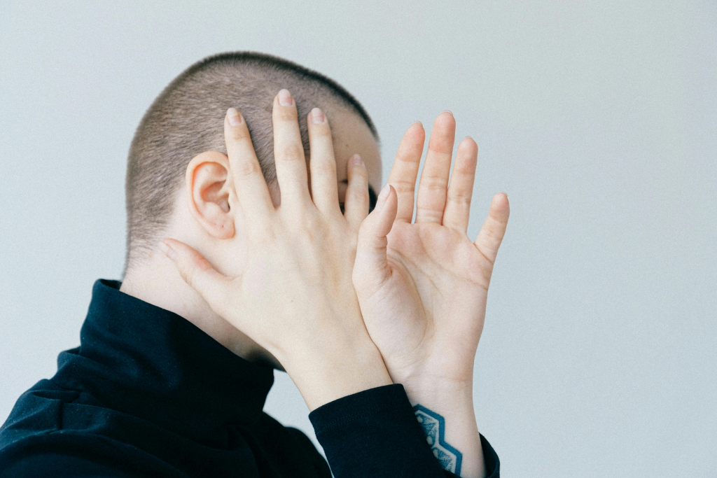 Person covering their face with both hands in a gesture of shame or emotional overwhelm.
