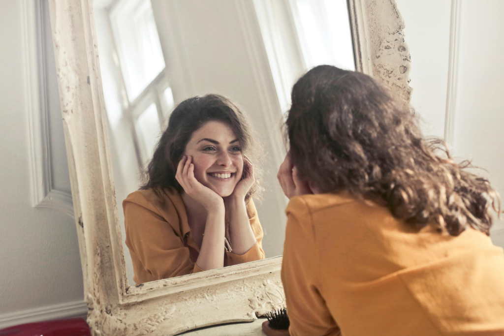 Person genuinely smiling at their reflection in a mirror, representing self-acceptance and healing.