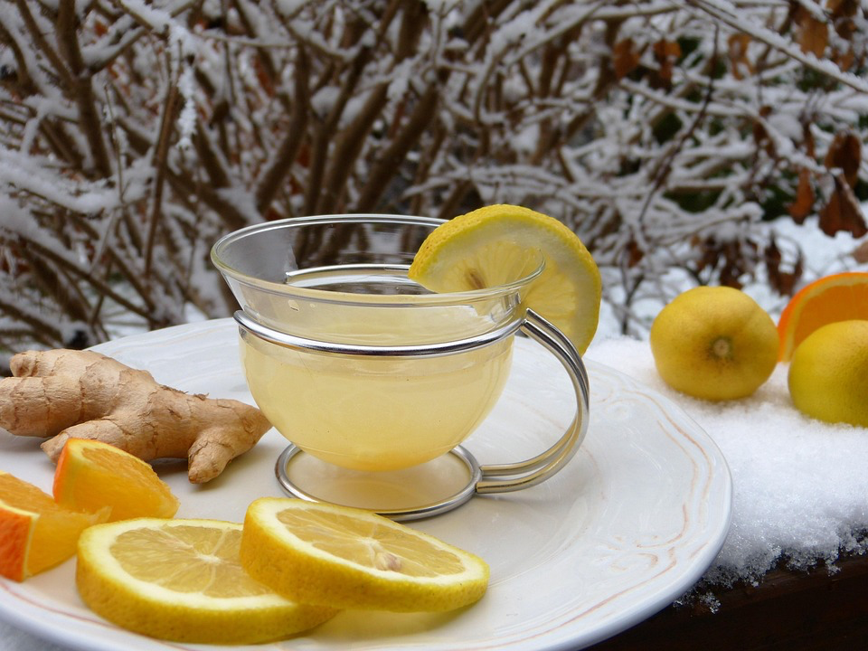 Warming ginger-lemon tea in a clear mug, surrounded by fresh citrus and ginger root in a snowy winter setting.