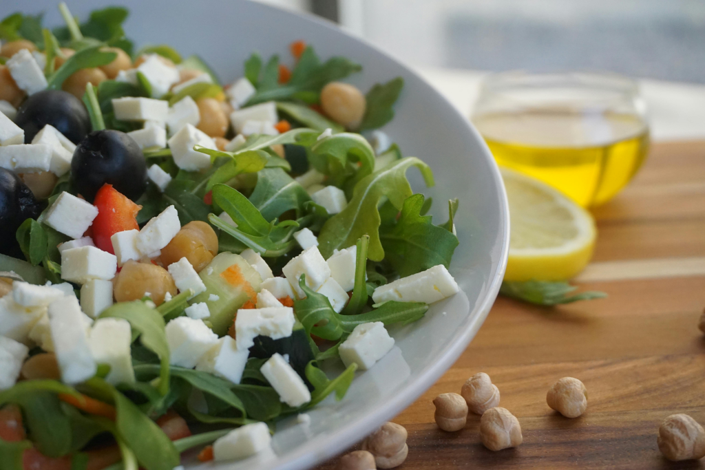 Colorful salad bowl filled with mixed greens, white cheese cubes, and nuts, with lemon and olive oil nearby.