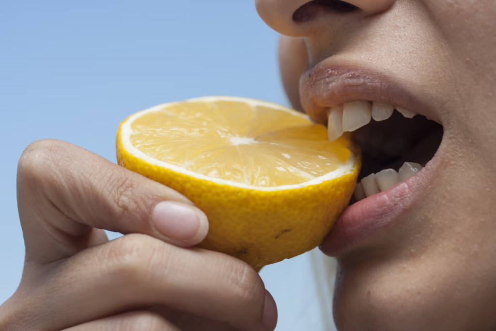 Person taking a big bite of a fresh lemon slice.