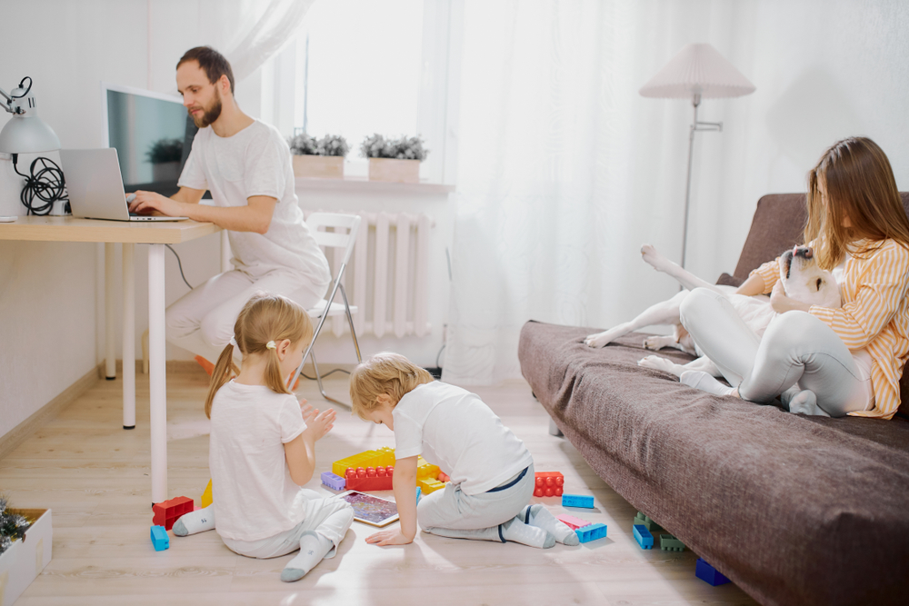 family together at home, spend free time, holiday in living room, have a rest. Child girl play with toys, woman petting their domestic dog, while man sit working on laptop, work from home
