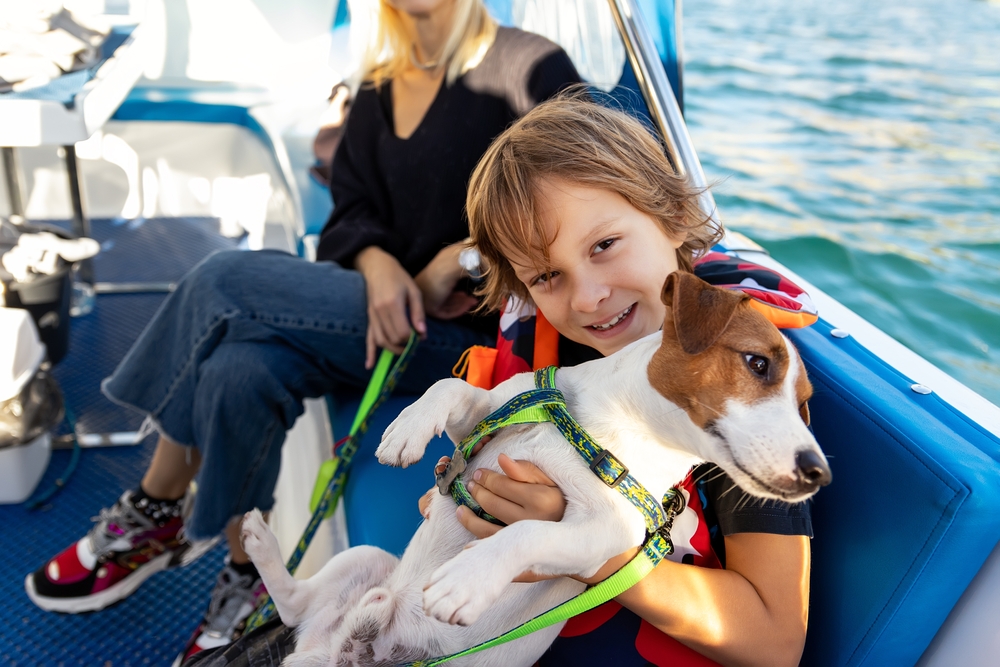Portrait of cute liitle boy child enjoy petting cute adorable little jack russel dog puppy sailing family luxury yacht boat against blue water bright sunny summer day. Travel sea tourism with pets
