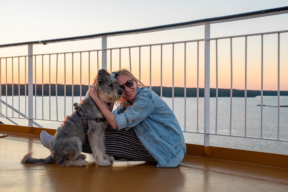 Young woman sitting on a deck of a cruise ship with her dog.
