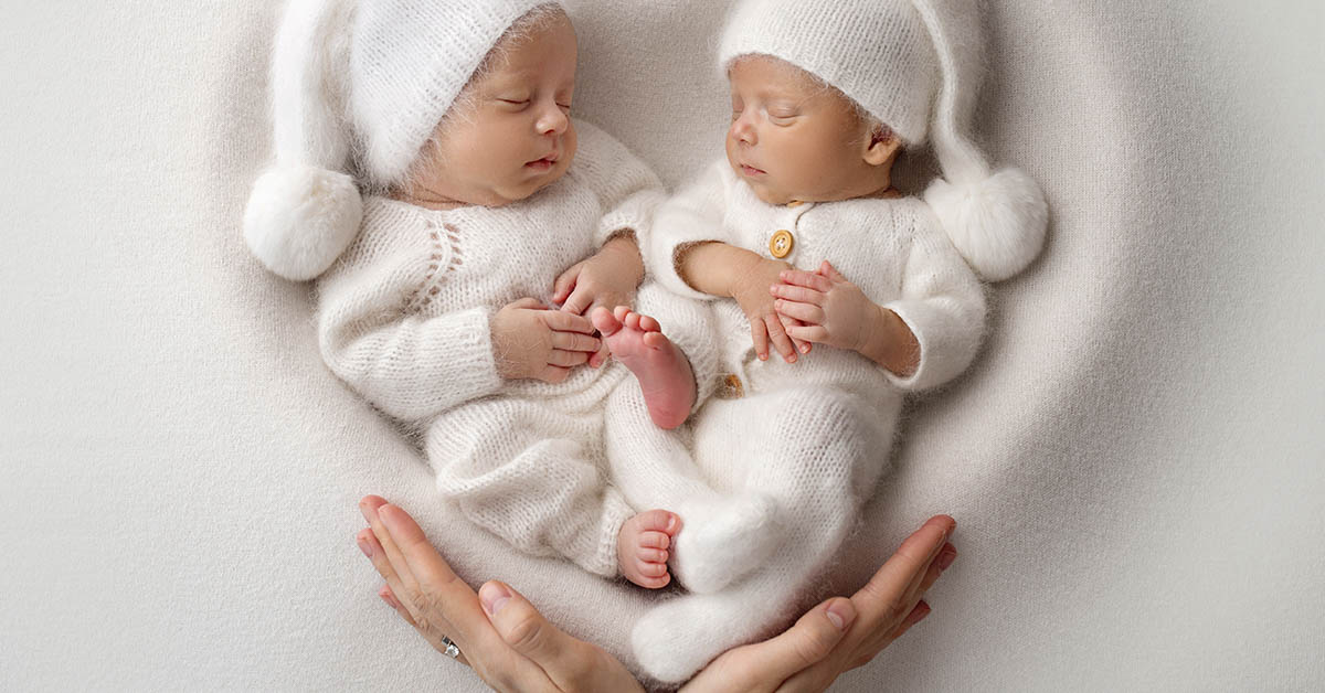 Twin babies wearing all white placed inside a heart shaped surface