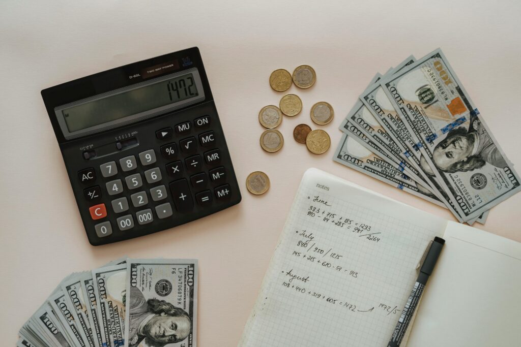 Calculator, cash bills, coins, and handwritten notes spread on a white surface.